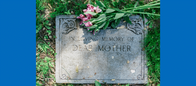 Gravestone reading 'In Loving Memory of Dear Mother' with a bouquet of pink flowers laid on top, surrounded by green grass.